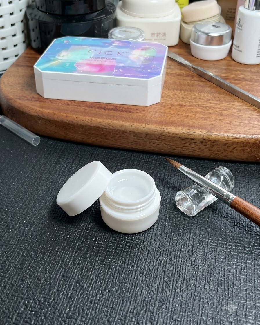 Un frasco de gel base transparente colocado sobre una mesa junto a un pincel fino para nail art y una caja de almacenamiento cosmético.