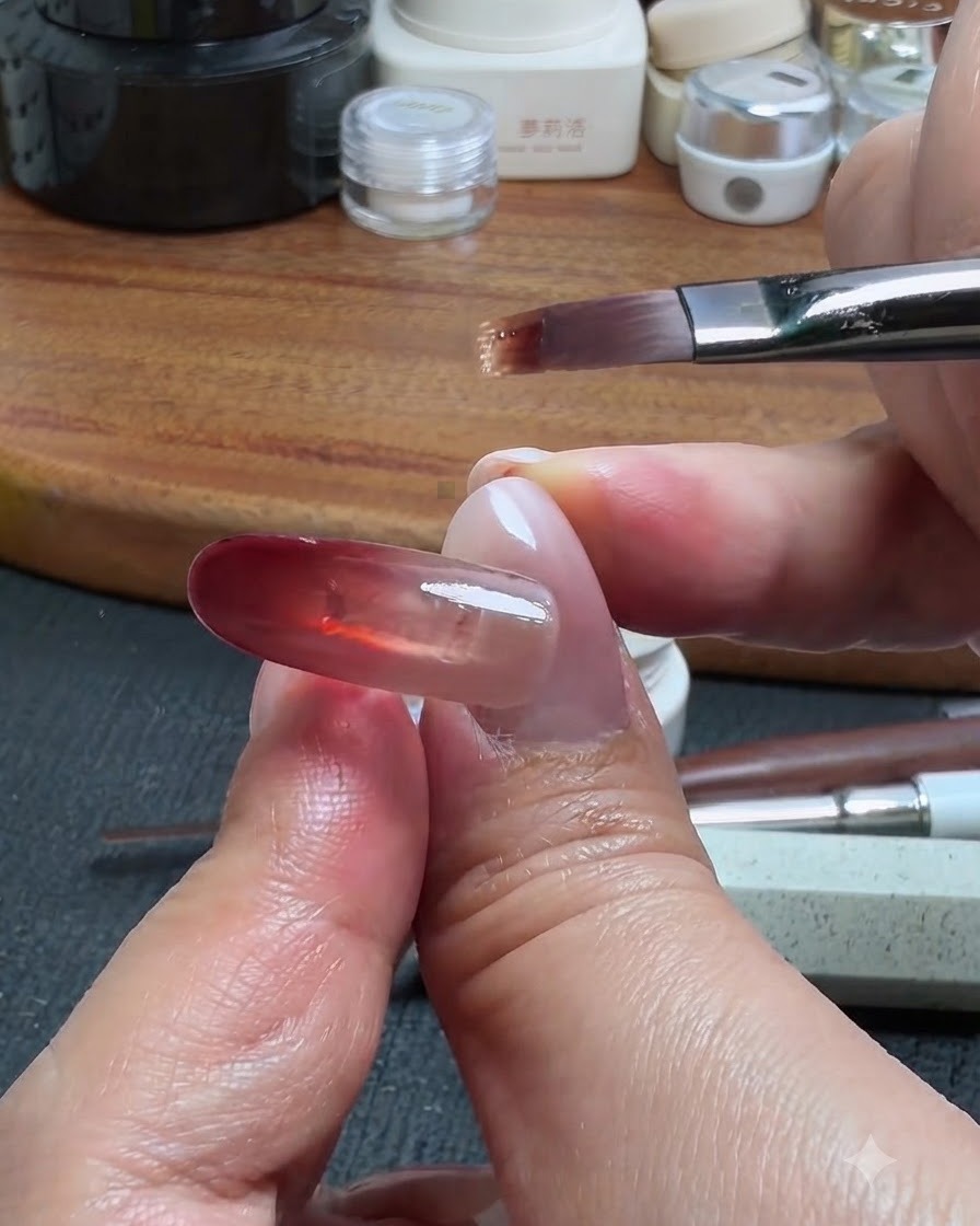 Un pincel de uñas tomando una cantidad diminuta de gel base para arrastrarla hacia arriba desde el bloque rojo, creando un efecto degradado ombré.