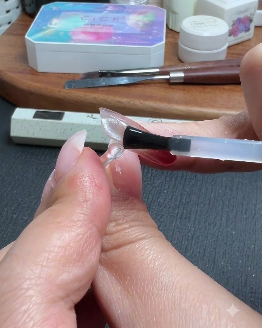 Un pincel aplicando una capa de top coat sobre una extensión de uña translúcida y transparente.