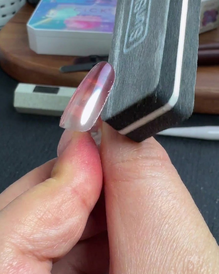 Una lima de uñas dando forma al borde lateral de una uña cromada terminada.