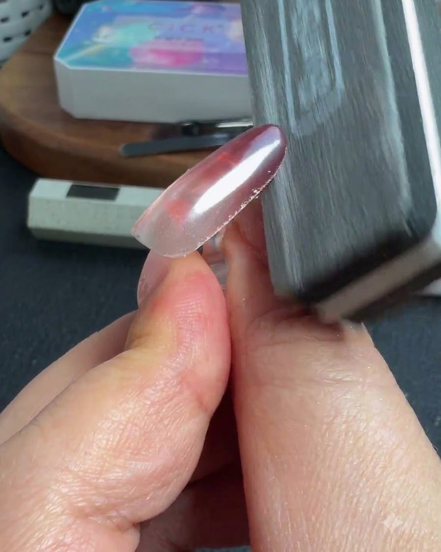 Una esponja o lima de uñas limpiando el exceso de polvo del borde de una uña brillante.
