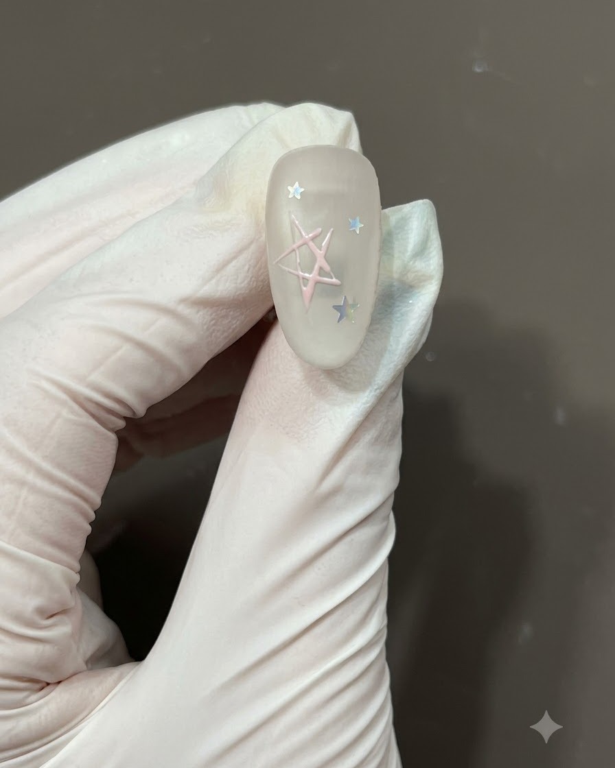 Un pincel fino de nail art rellenando el centro del contorno de una estrella dibujada a mano con esmalte en gel rosa claro sobre una uña mate.