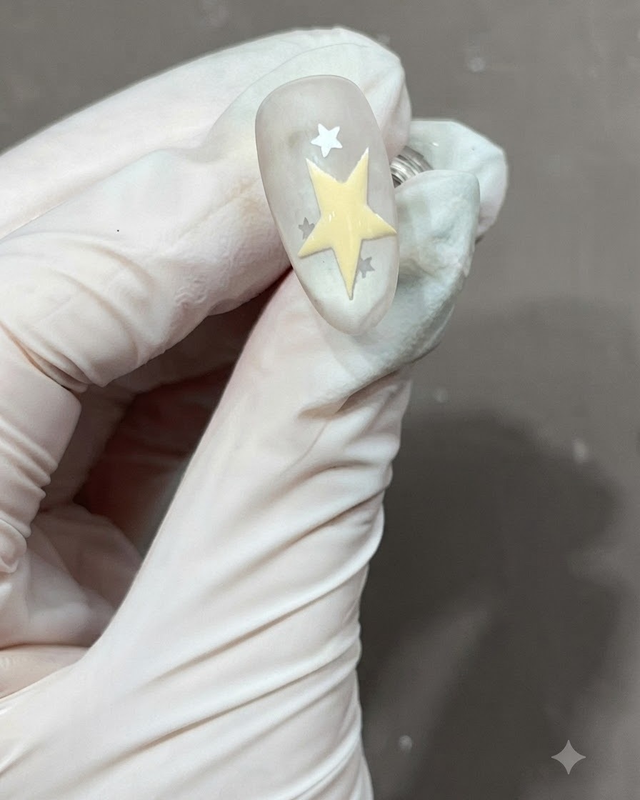 Una estrella de cinco puntas amarilla recién dibujada y rellenada junto a otras estrellas en una uña mate.