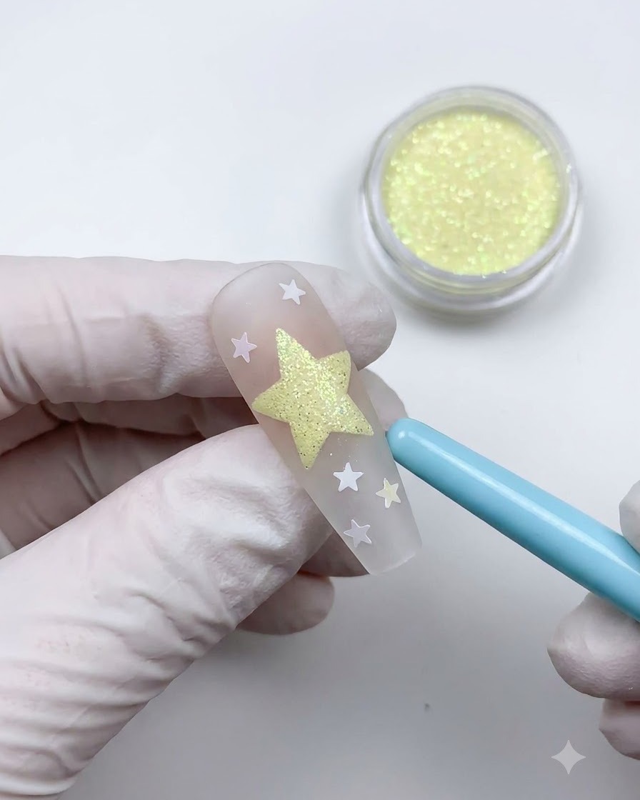 Un pincel plumero azul suave barriendo el polvo suelto para revelar un diseño de arte de uñas de estrellas texturizadas.