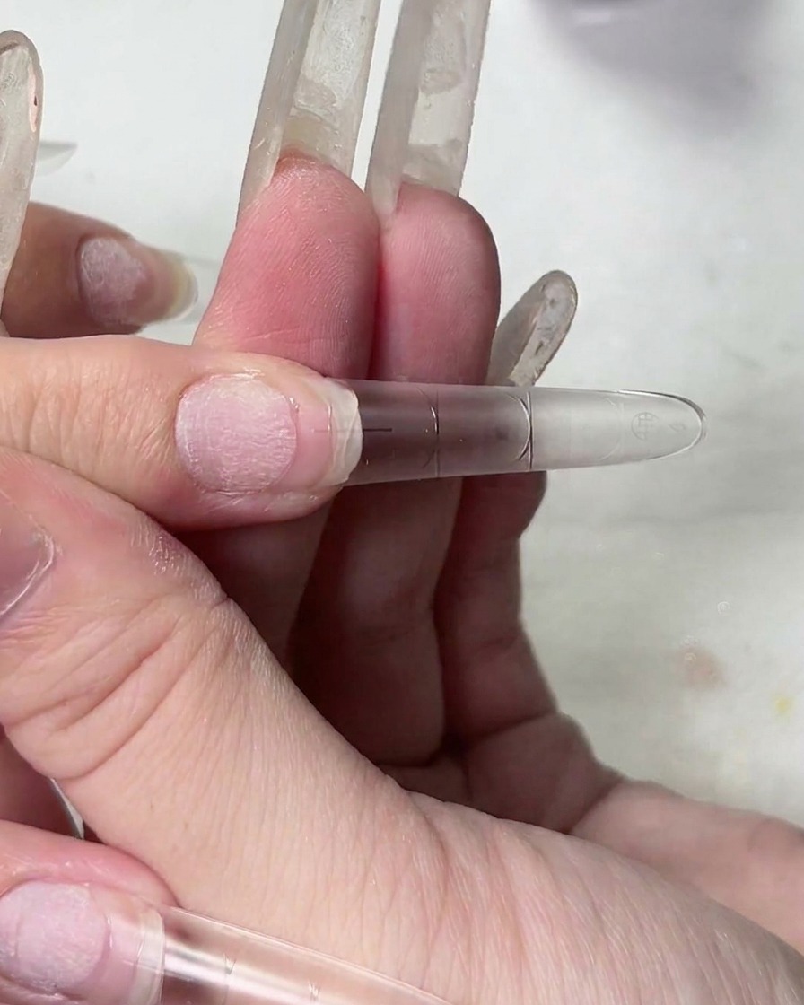 Primer plano de una mano levantando un tip de uña, mostrando la textura elástica del gel adhesivo transparente.