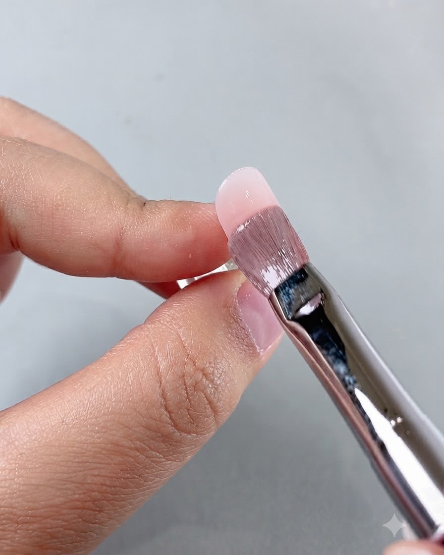 Un pincel de manicura alisando producto cerca del área de la cutícula mientras trabaja en la aplicación de la uña.