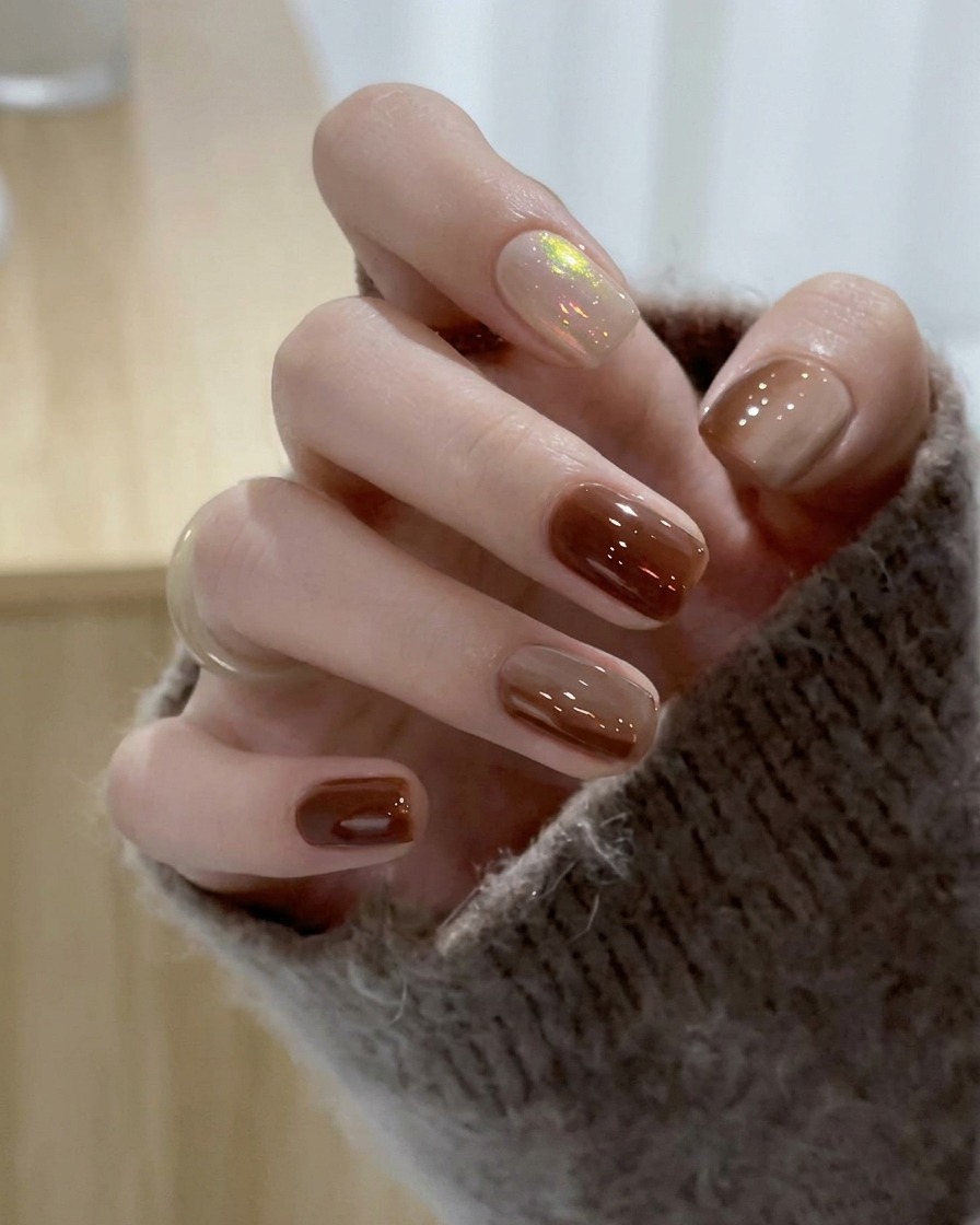 Un pincel deslizando esmalte en gel nude translúcido sobre la uña del dedo medio.