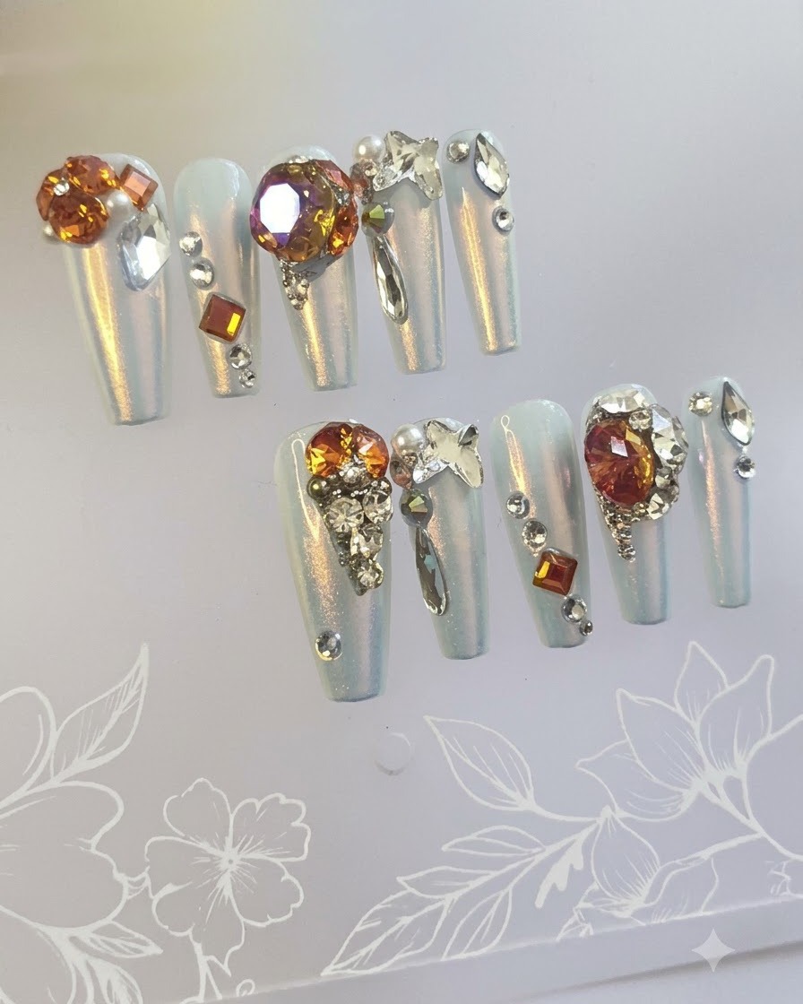 Macrofotografía centrada en las uñas decorativas destacadas con fondos degradados de ámbar y cúmulos de grandes piedras de joyería brillantes.