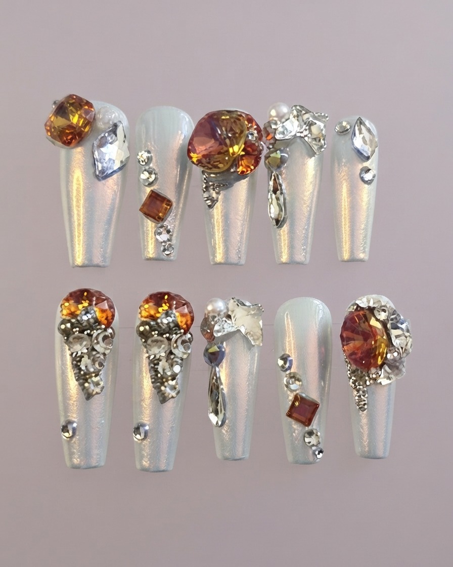 Toma detallada de una uña postiza del pulgar decorada que presenta una gema ámbar prominente rodeada de cristales transparentes.