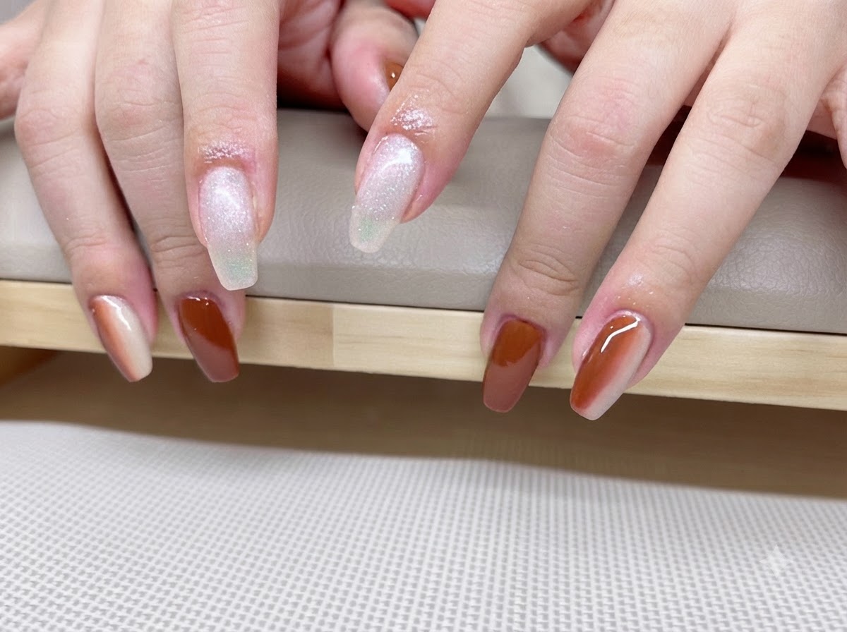 Una vista de cerca de manos que muestra una manicura degradada en caramelo y ámbar con líneas brillantes de efecto ojo de gato.