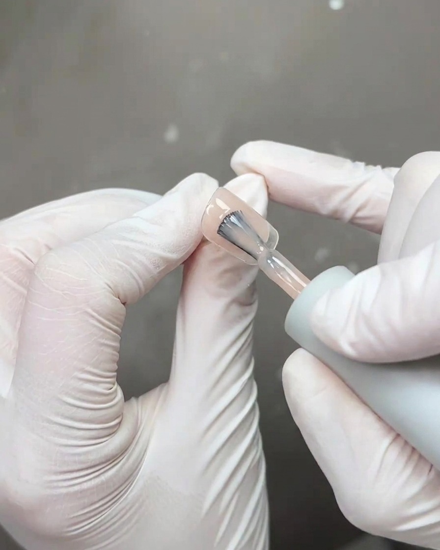 Un pincel aplicando una capa gruesa de esmalte protector transparente y brillante sobre el arte de uñas terminado.