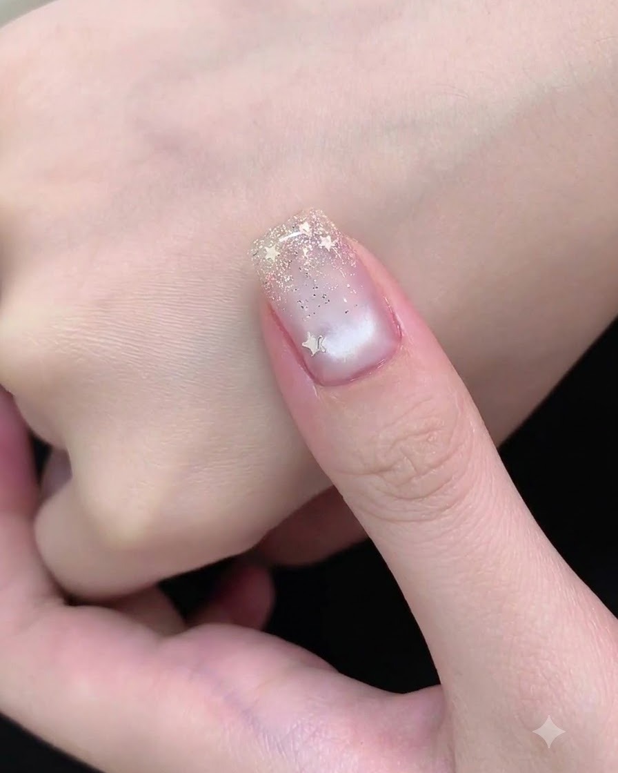 Un pincel de arte de uñas aplicando brillo plateado fino en el borde libre de la uña para formar un degradado.