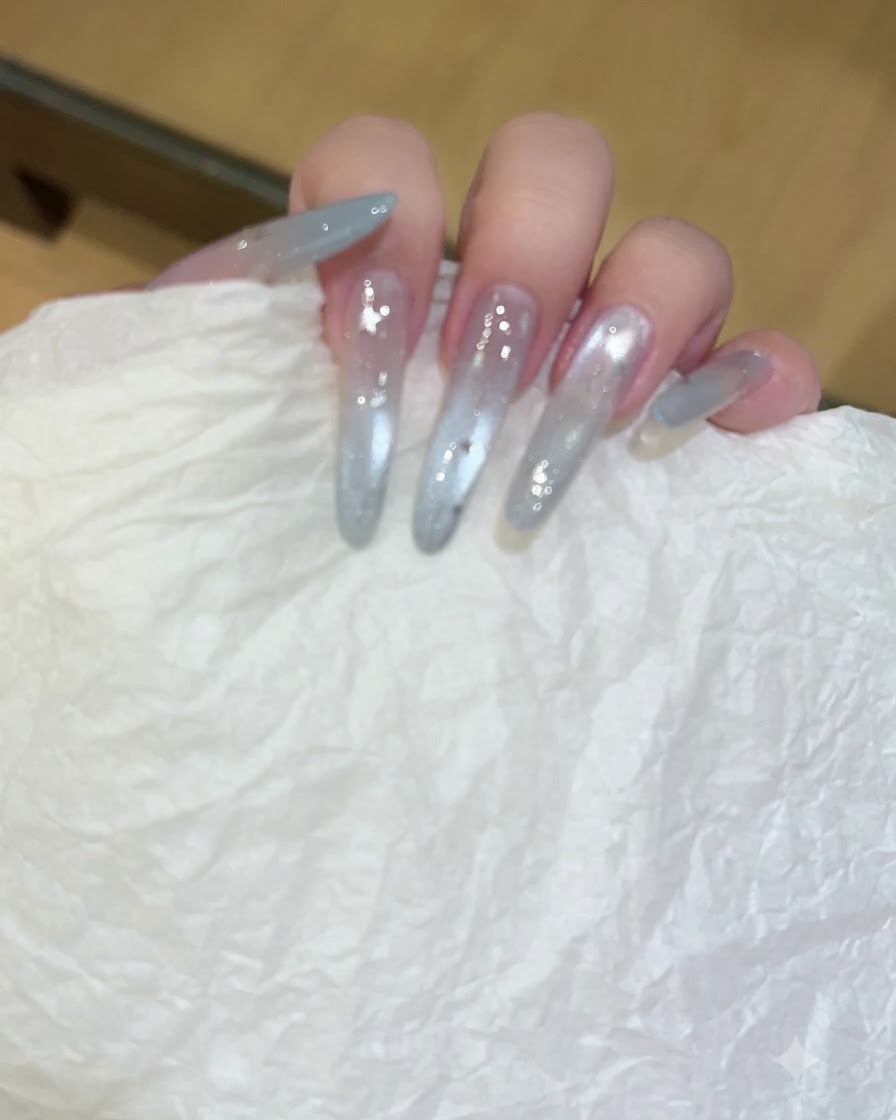 Una mano sosteniendo un pañuelo texturizado blanco limpiando uñas largas y traslúcidas con extensión de gel.