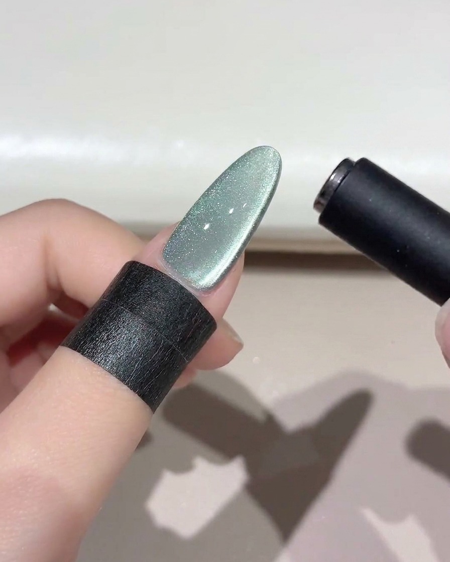Una herramienta magnética negra flotando sobre una uña brillante de ojo de gato verde para dar forma a la banda de luz.