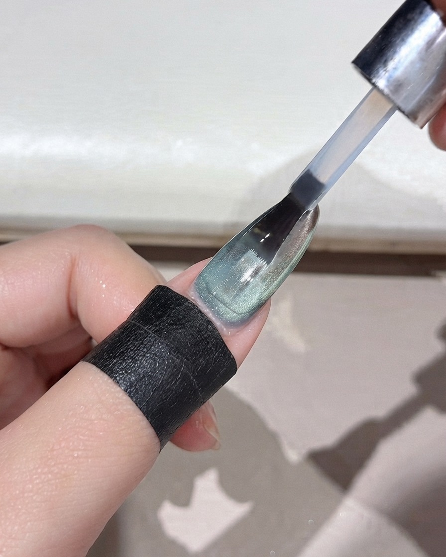 Un pincel de uñas aplicando una capa superior transparente sobre una uña con degradado en polvo verde y acabado espejo.