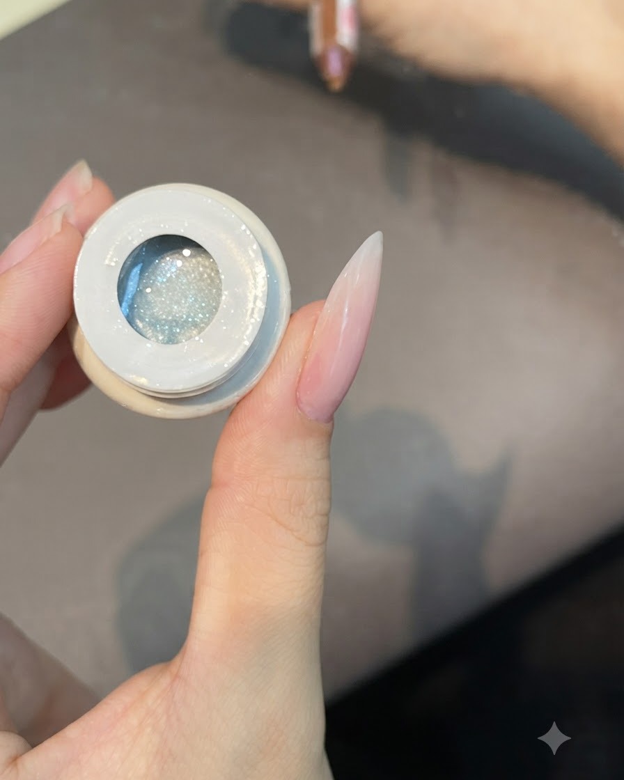 Un pincel plano sumergiéndose en un frasco abierto de esmalte de gel translúcido de ojo de gato número 49.