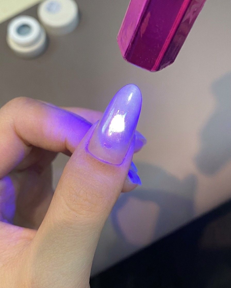 Una lámpara UV portátil de color morado brillando con luz brillante sobre un dedo manicurado para curar la capa de gel.