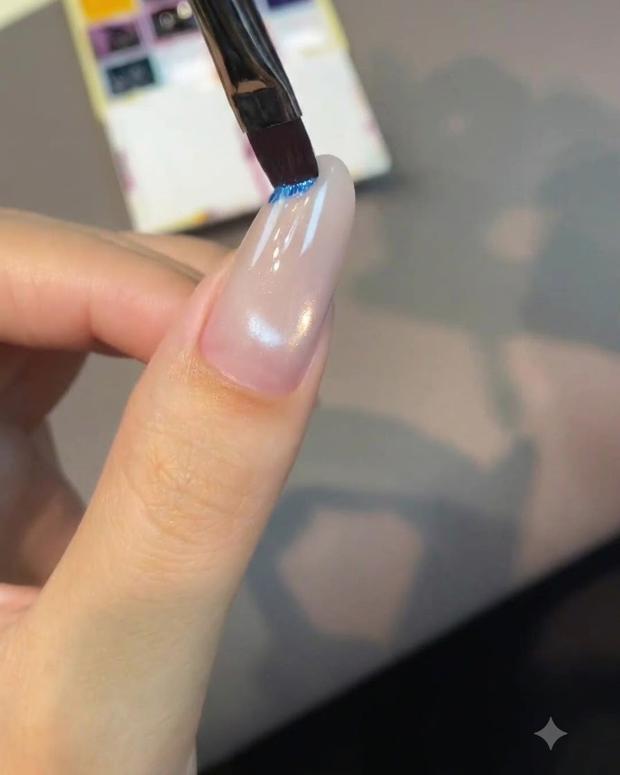 Un pincel plano de arte de uñas sumergiéndose en una bandeja de pigmento azul brillante sobre una paleta.
