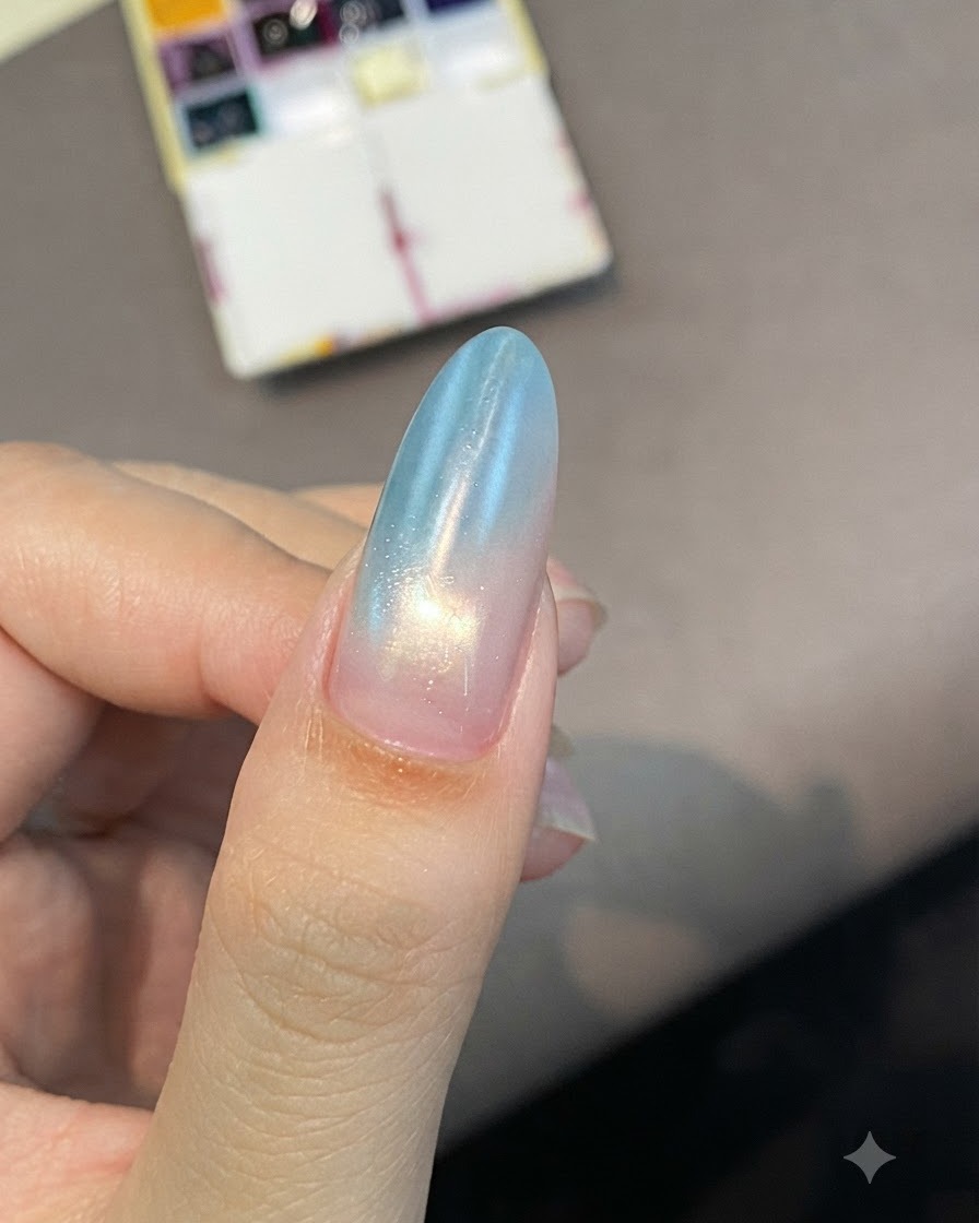 Una uña en forma de almendra con un degradado suave de azul a rosa, mostrando un brillo de curado bajo la iluminación.