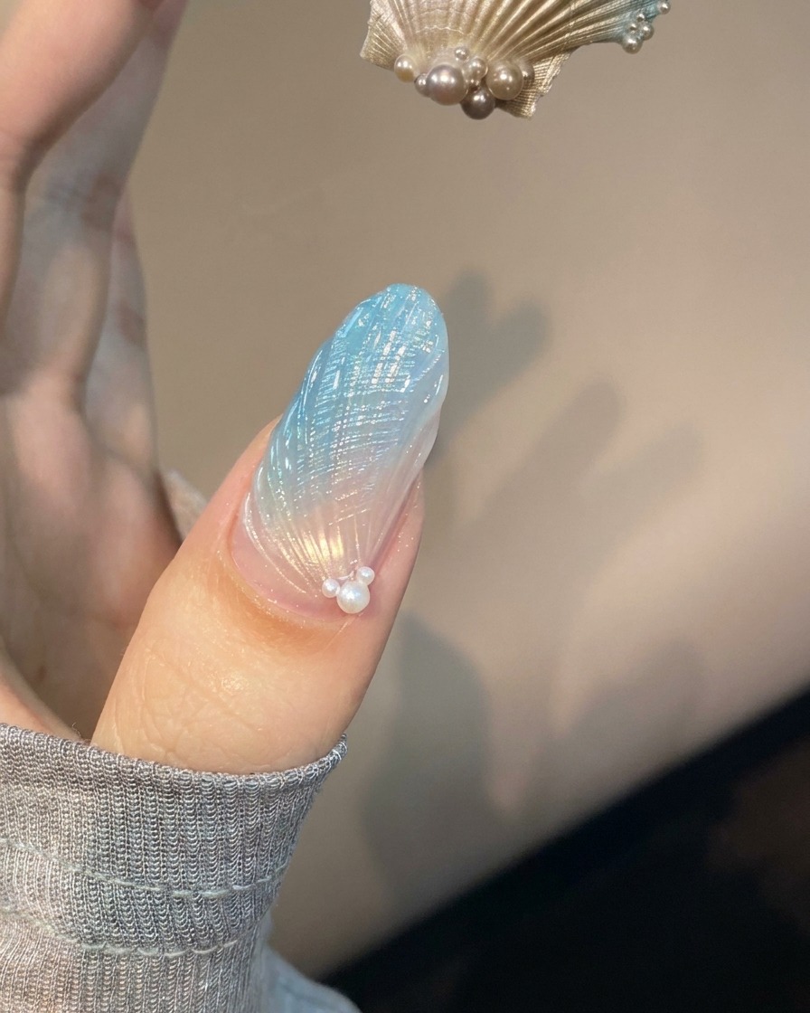 Una uña con arte de uñas de concha azul y translúcida colocada bajo una lámpara UV morada curándose.
