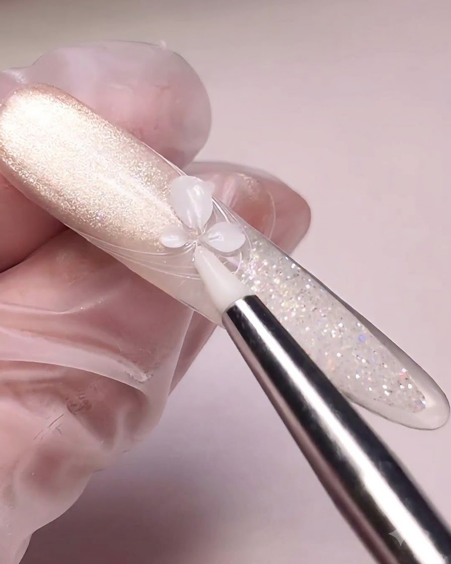 Una herramienta de silicona presionando gel blanco de esculpido formando pétalos de flor sobre un tip de uña pintado con efecto ojo de gato.