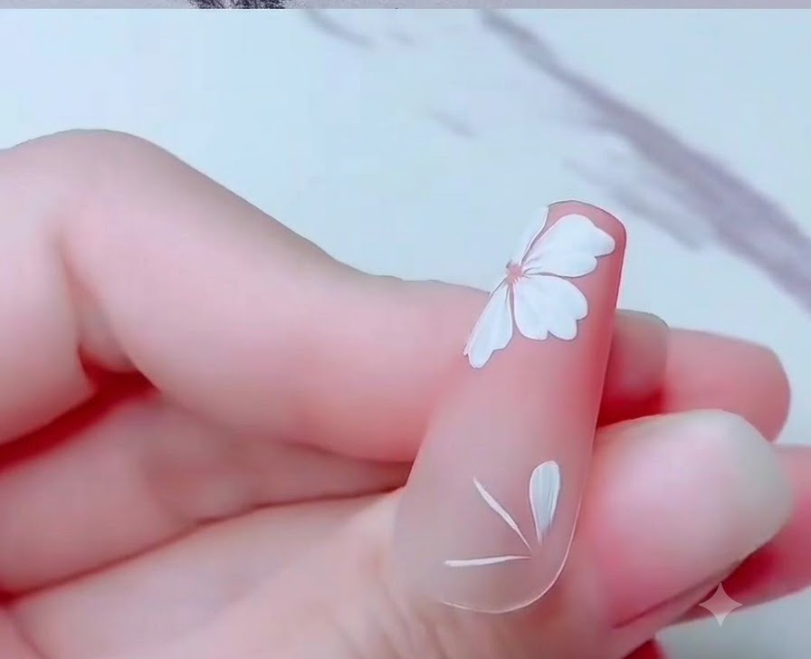 Primer plano de una uña que muestra pétalos parciales de flor de cerezo pintados cerca del borde inferior.