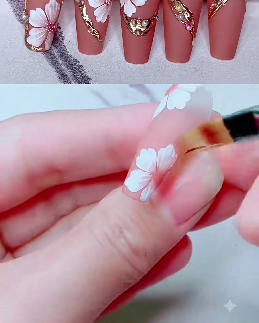 Un pincel de difuminado pequeño mezclando color rosa sobre pétalos de flores pintados de blanco en una uña.