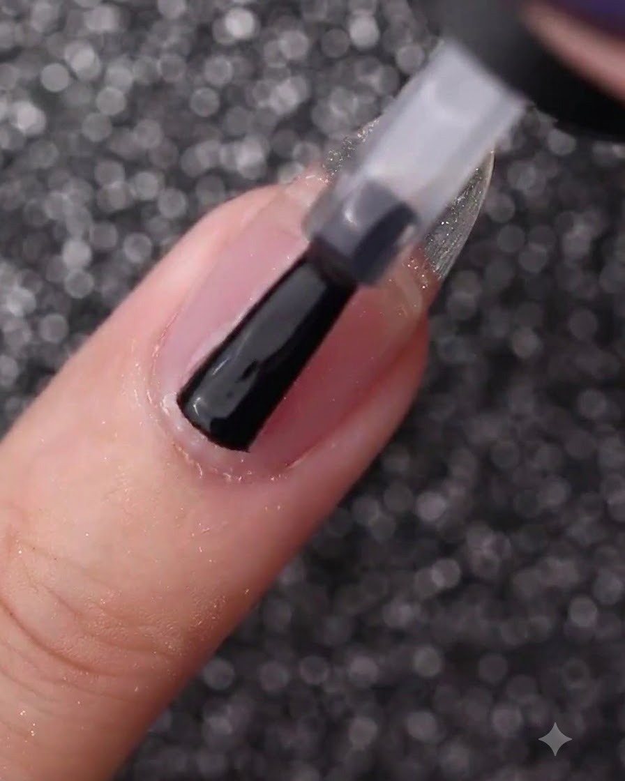 Una mano usando el pincel de un frasco para cubrir una uña natural sin esmalte con gel base transparente.