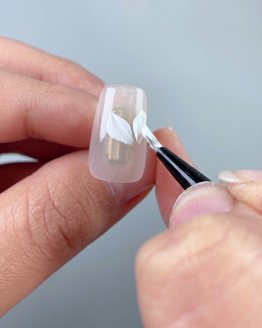 Un primer plano que muestra pétalos blancos más pequeños que se están pintando en la uña.