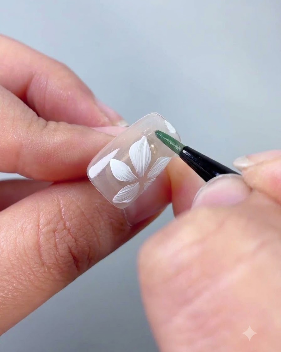 Un pincel delineador que aplica gel verde para formar una hoja delgada al lado de la flor blanca.