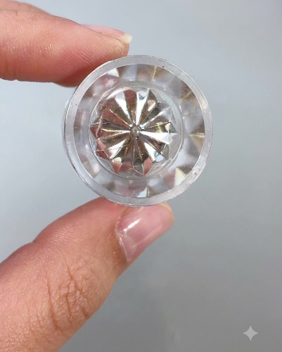 Una vista cercana de la parte superior de un recipiente de cristal transparente y facetado o una herramienta aplicadora que refleja la luz contra un fondo claro.