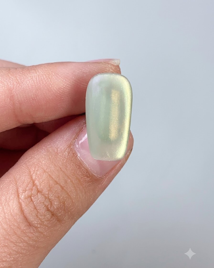 Un pincel de uñas que aplica una capa superior sobre una uña de gel ojo de gato verde.