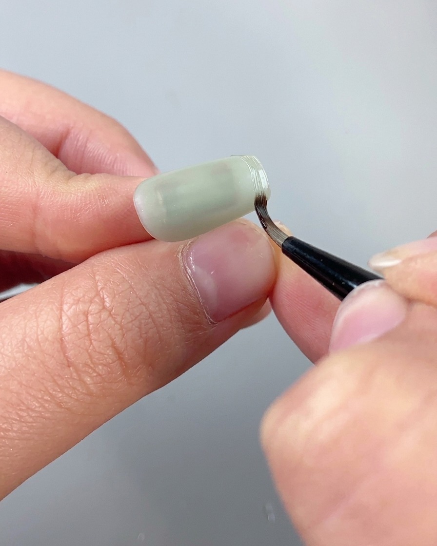 Un pincel de detalle fino que usa gel de escultura de textura transparente para trazar un borde elevado a lo largo del borde de una uña ojo de gato.