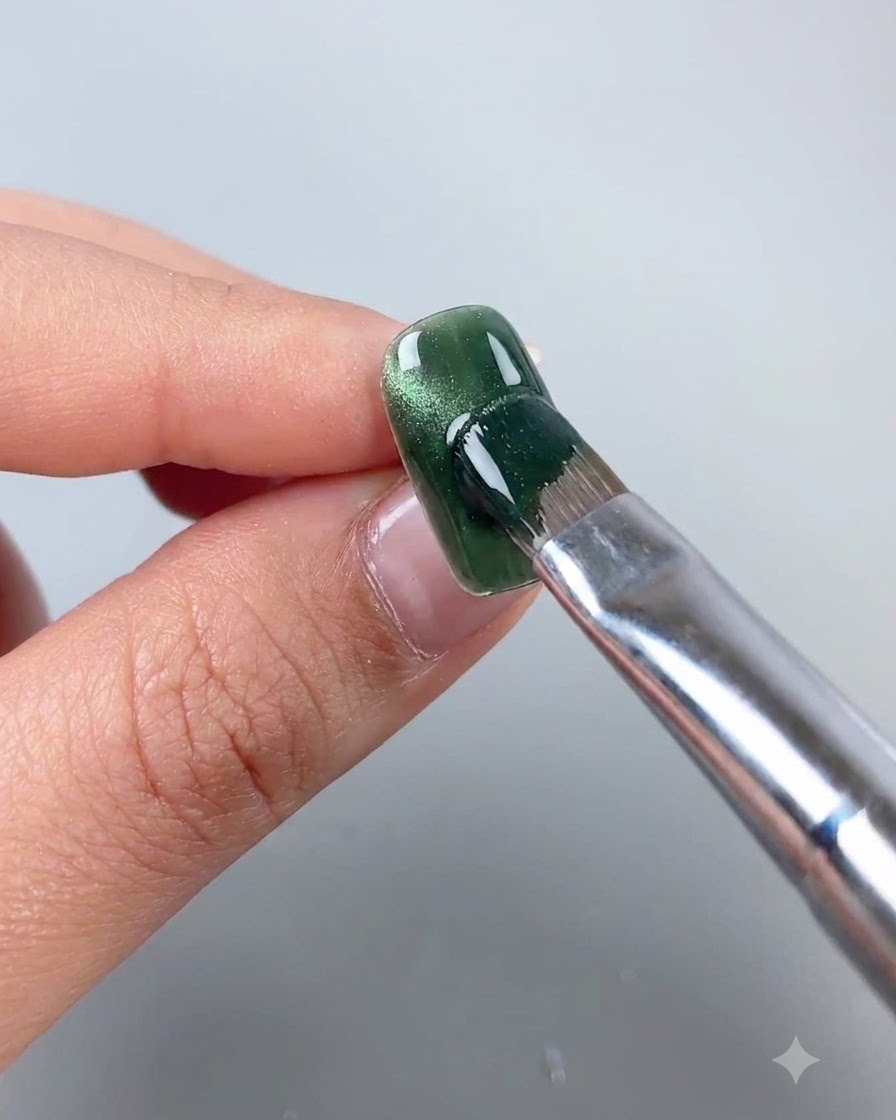 Una varita magnética sostenida cerca de una uña de gel ojo de gato verde para cambiar las partículas magnéticas a una línea de arco lateral.