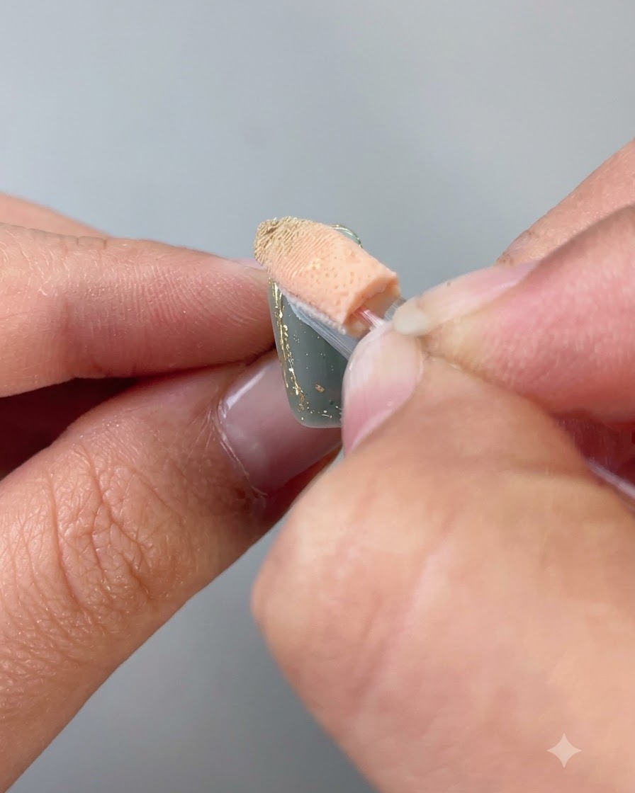 Un aplicador de esponja que frota polvo de oro en el contorno del borde de una uña.
