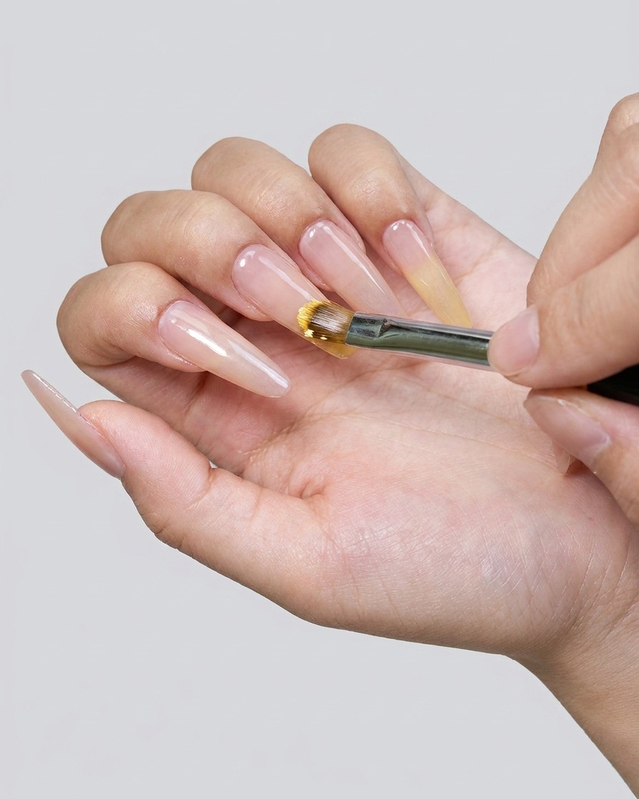 Primer plano de un pincel aplicando esmalte de gel amarillo en la punta de la uña.
