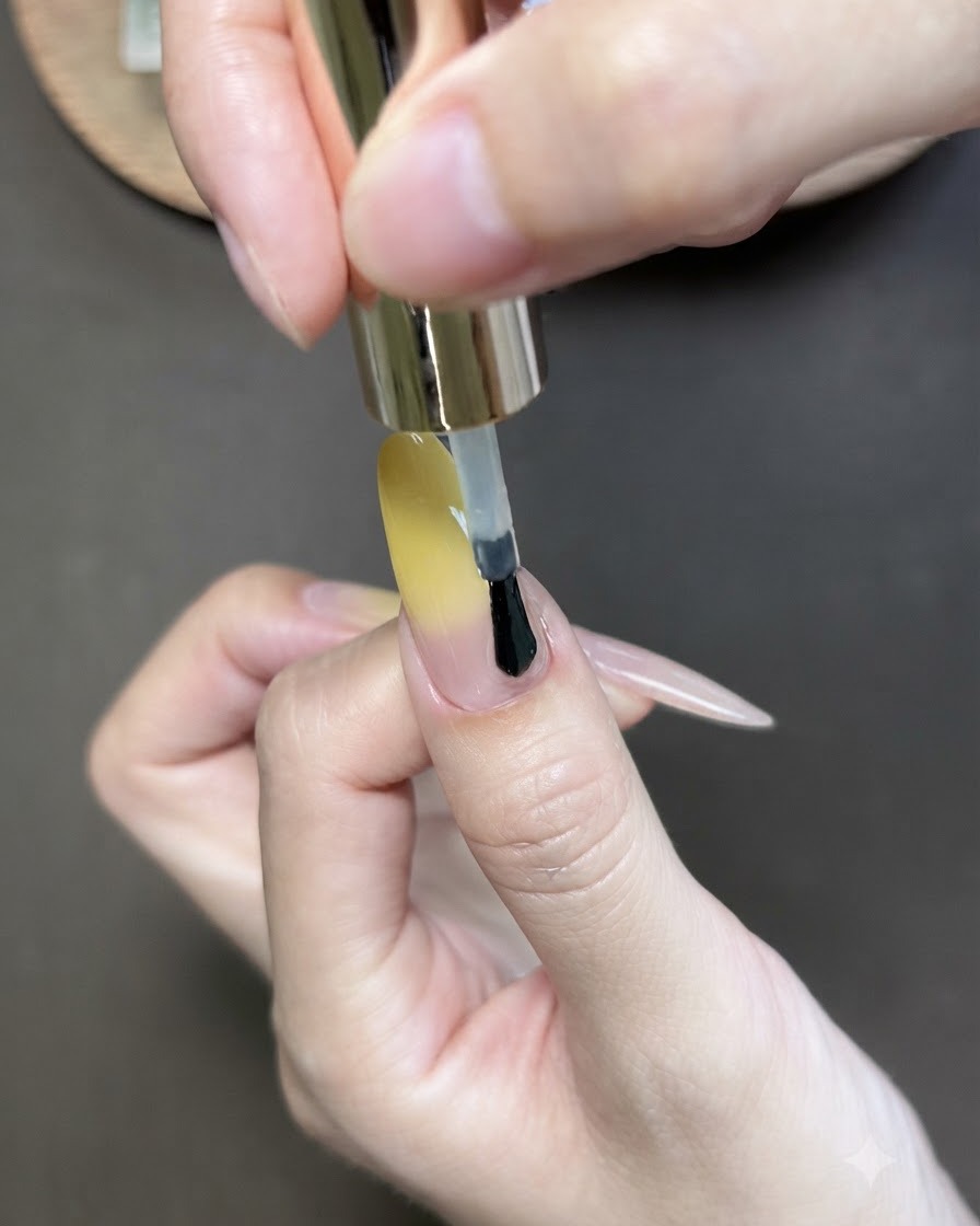 Un pincel aplicando esmalte de gel ojo de gato sobre la uña del pulgar con degradado amarillo.