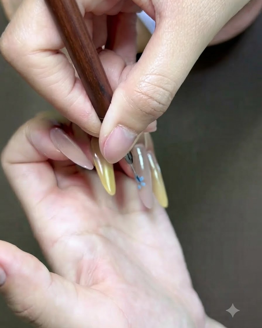 Primer plano detallado de un pincel fino de arte de uñas agregando un acento floral rosa en la uña.