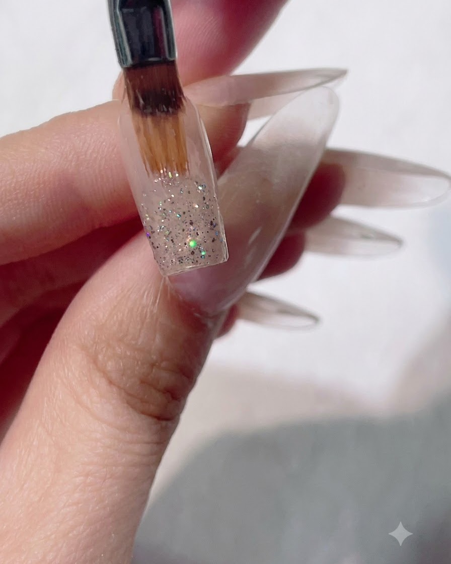 Un pincel de gel plano y suave barriendo la purpurina húmeda hacia abajo en una uña para crear un efecto de degradado ombré.