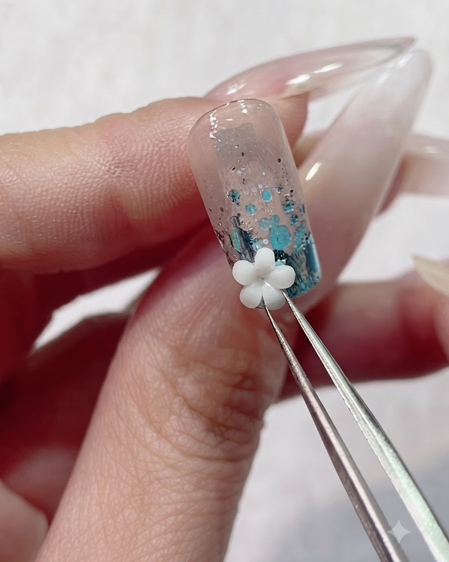 Pinzas de precisión colocando un dije de flor acrílica 3D blanca sobre el gel húmedo cerca de la cutícula de la uña.