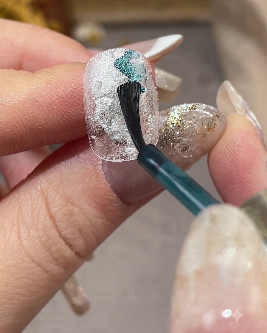 Un pincel de uñas aplicando líquido difuminado azul claro en diagonal sobre una uña blanca texturizada.