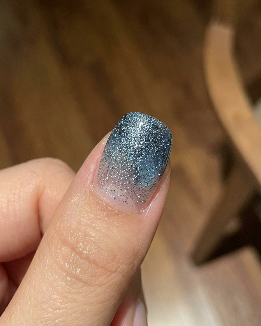 Un dedo mostrando una capa degradada de gel jelly azul translúcido sobre un fondo texturizado brillante, fotografiado con luz natural brillante.