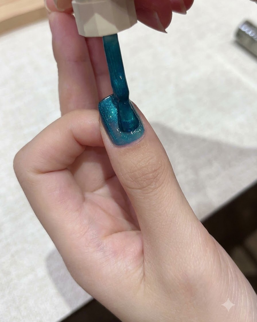 Un pincel aplicando esmalte de gel cat-eye azul verdoso vibrante sobre la superficie de una uña.
