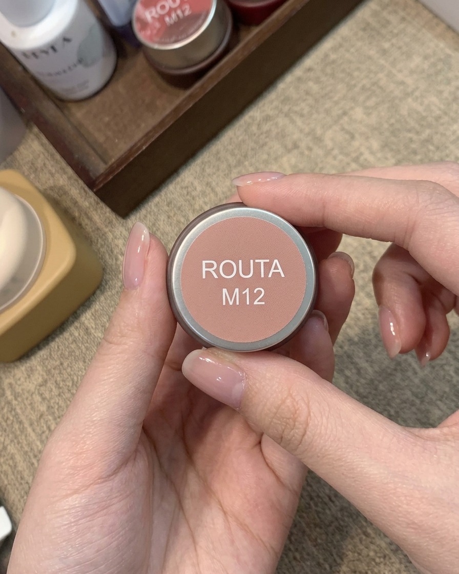 Un frasco pequeño etiquetado como Routa M12 que contiene un color de gel rubor rosa durazno cálido.