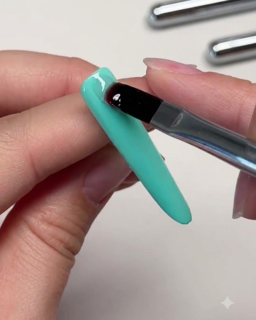 Un pincel colocando una perla transparente de gel de refuerzo en la sección superior de una uña verde menta para construir el ápice.