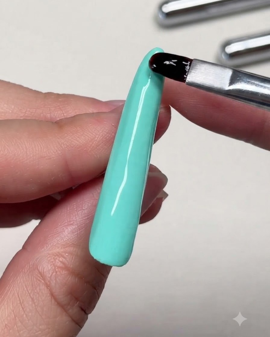 Un primer plano de un pincel nivelando el gel de refuerzo cerca de la punta de una extensión de uña larga.