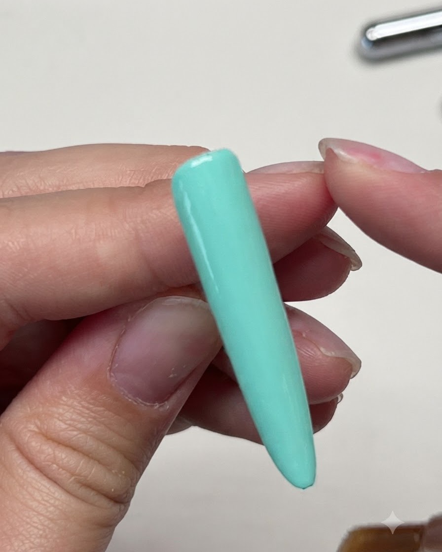 Un pincel aplicando un top coat mate sobre la extensión de uña sólida de color verde menta.