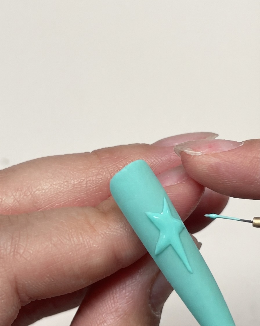 Una toma detallada de un contorno de estrella en gel completado en una uña verde menta antes de la aplicación de la textura.