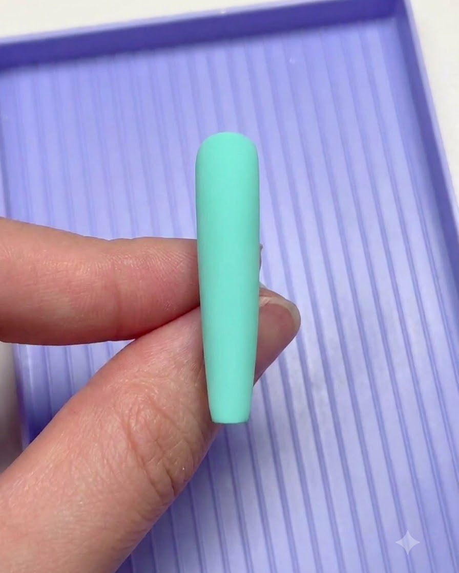 Una mano sosteniendo una uña verde menta sobre una bandeja de clasificación morada durante el diseño de nail art.