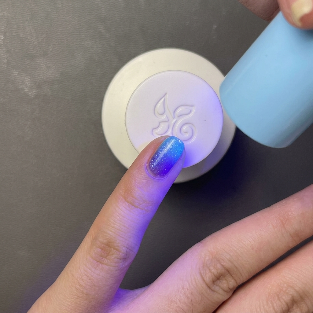 Un dedo con esmalte de gel azul brillante curándose bajo una lámpara UV/LED pequeña y portátil de color azul claro.